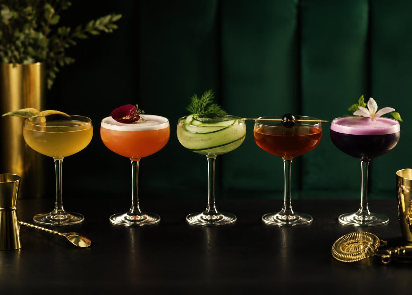 Row of signature craft cocktails garnished with edible flowers